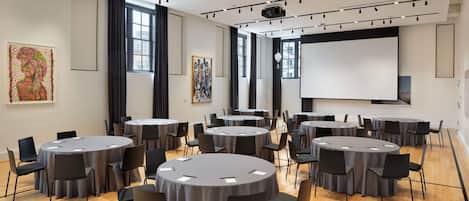Un salón de conferencias con varias mesas redondas, sillas, una pantalla de proyector y obras de arte en las paredes.