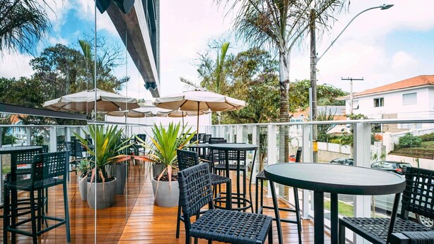Un patio al aire libre con piso de madera, sillas de mimbre negro y mesas. Hay sombrillas que dan sombra, y plantas en macetas decoran el área de estar.