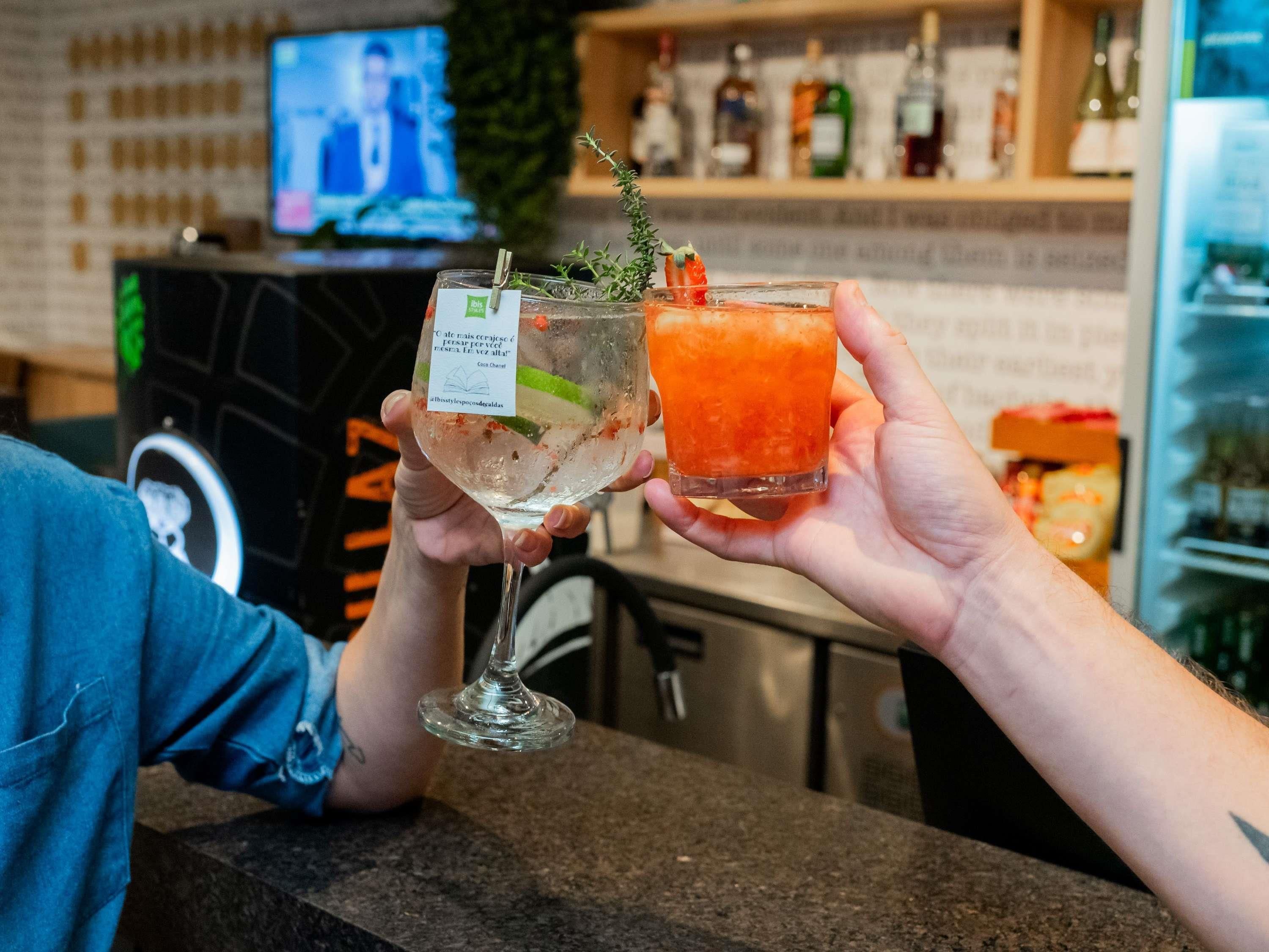Dos personas sosteniendo bebidas en un bar con un televisor al fondo.