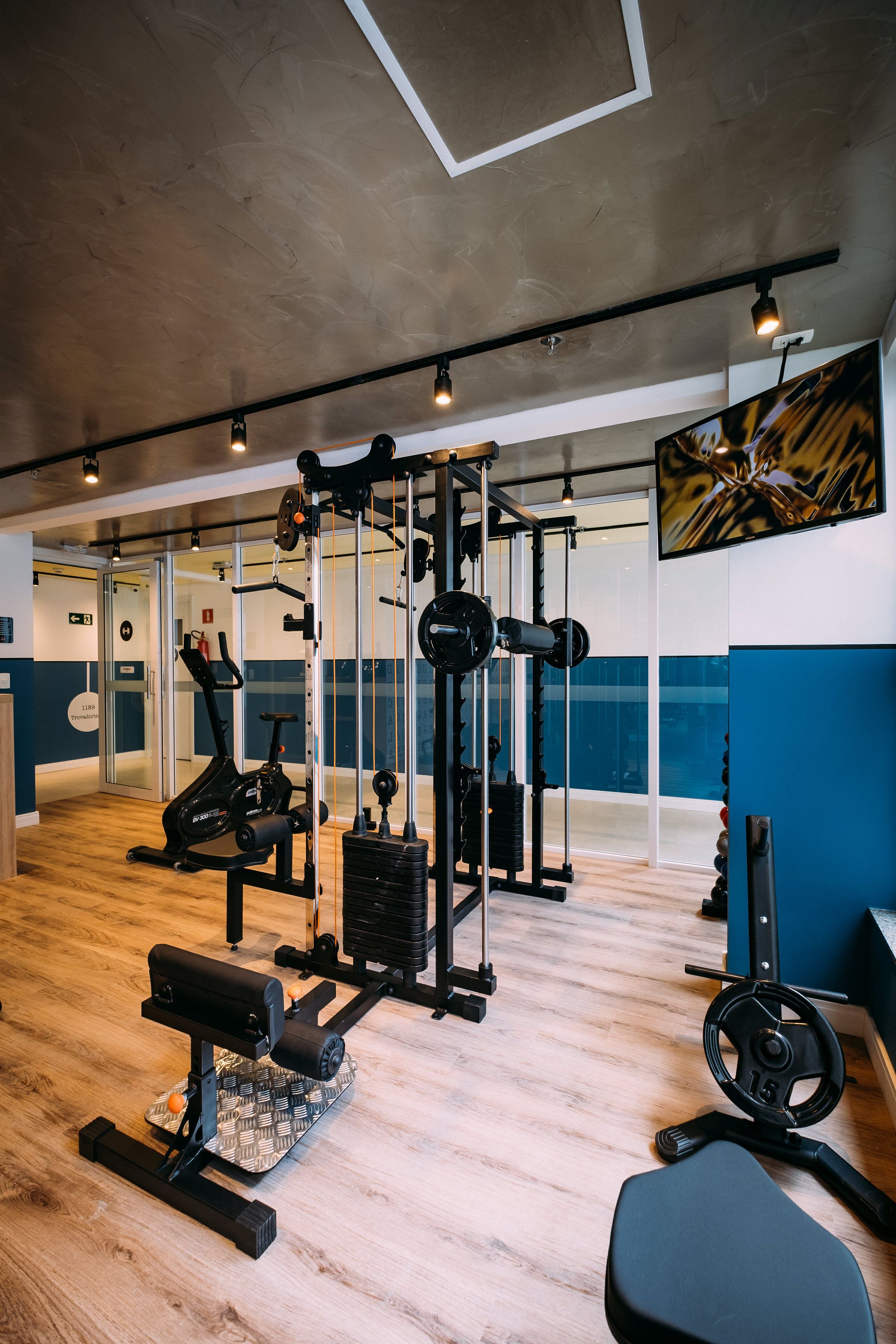 A gym with various exercise equipment, a large mirror, and a television on the wall.