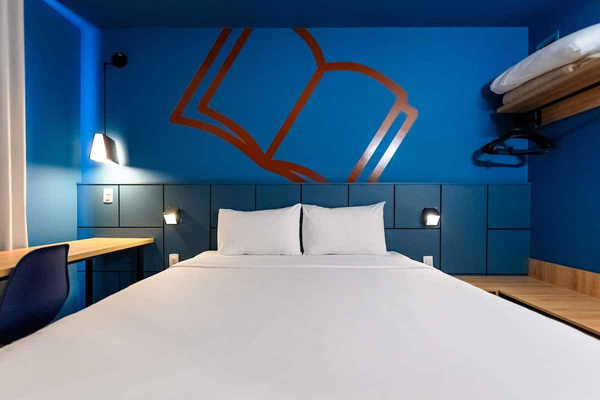 A hotel room with a large bed, two bedside tables, a desk, and a wall-mounted shelf.