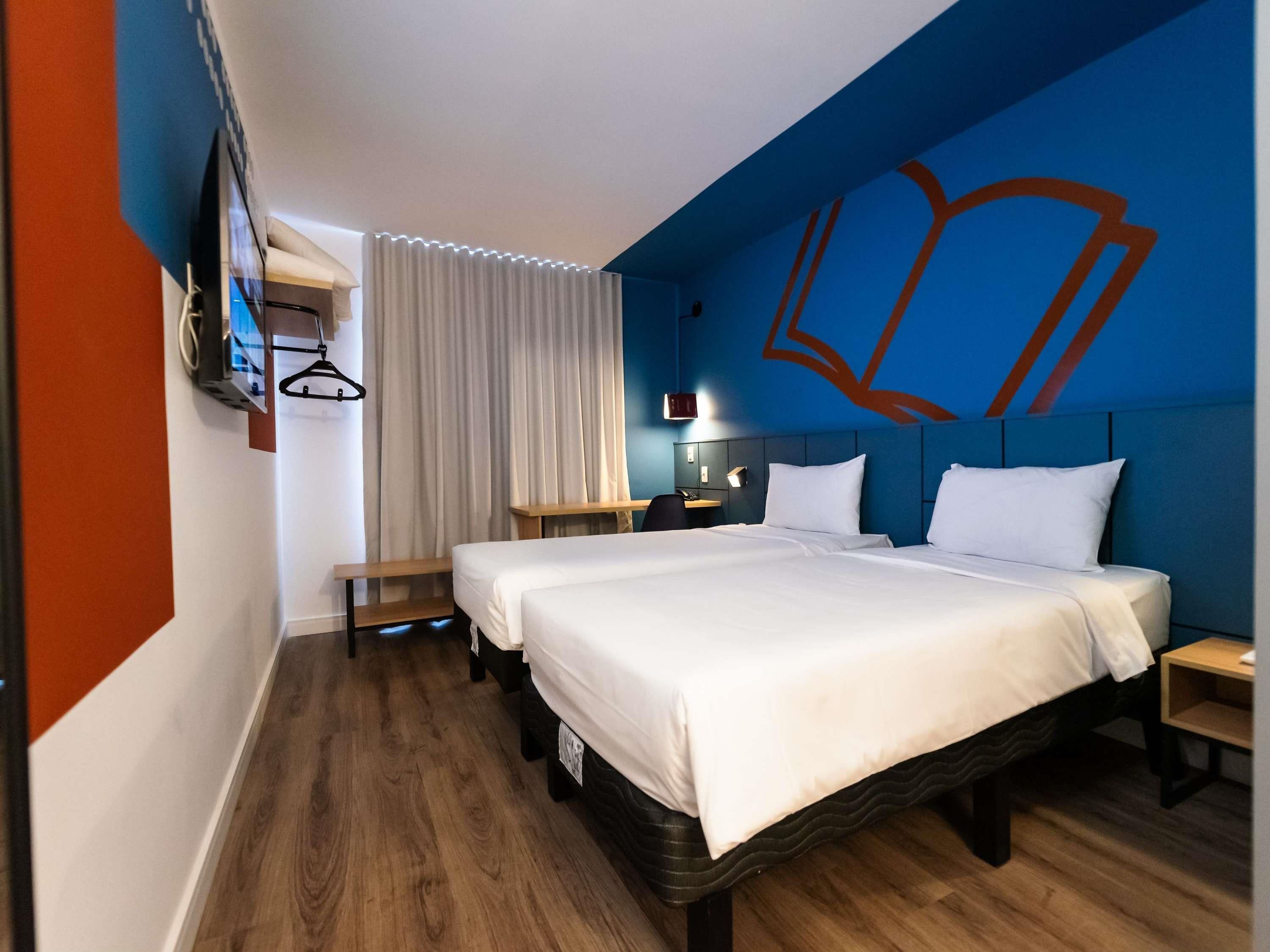 Een hotelkamer met twee bedden, een bureau, een stoel, een televisie en een gordijn.