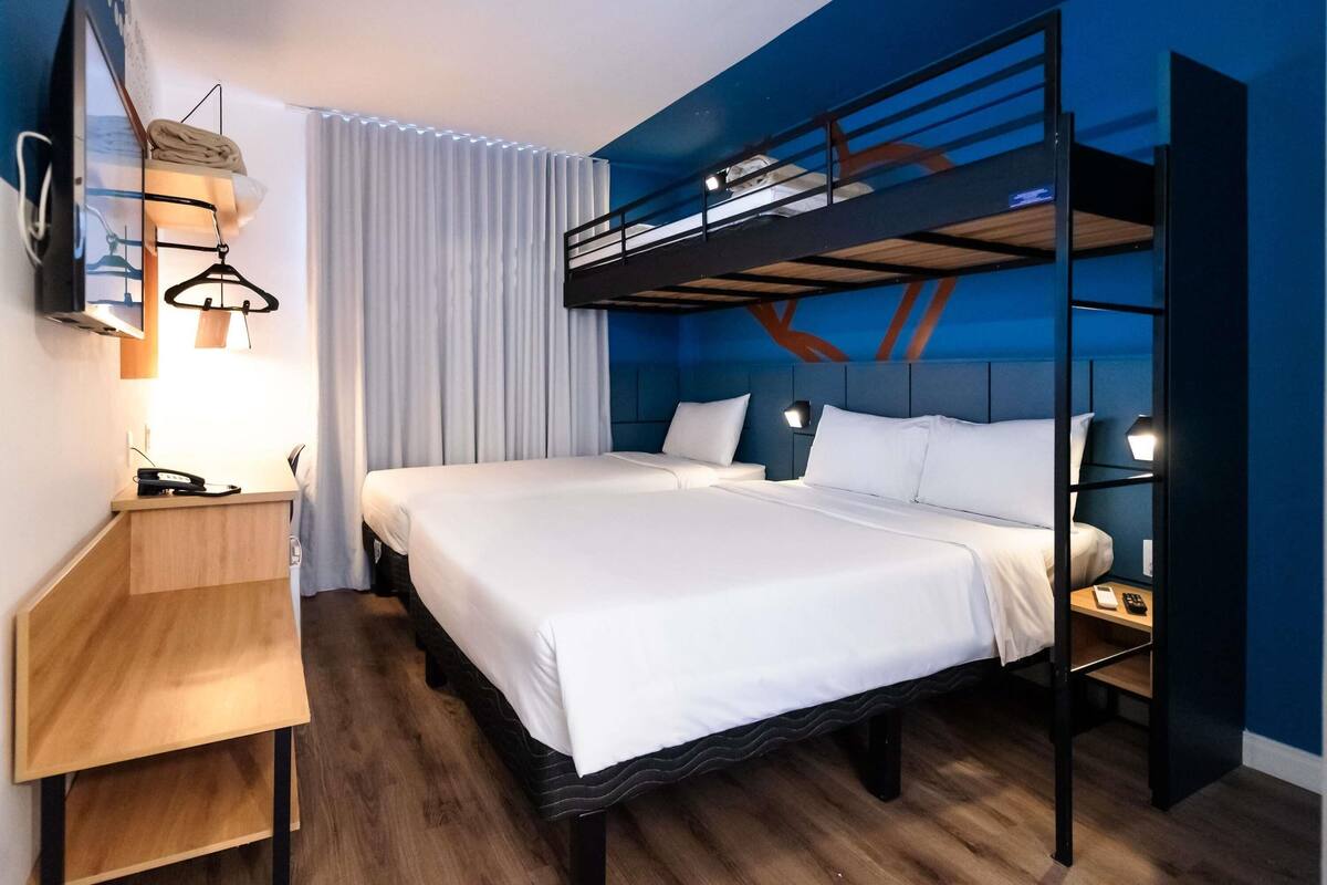 Una habitación de hotel con una cama litera, un escritorio con teléfono y un televisor montado en la pared.