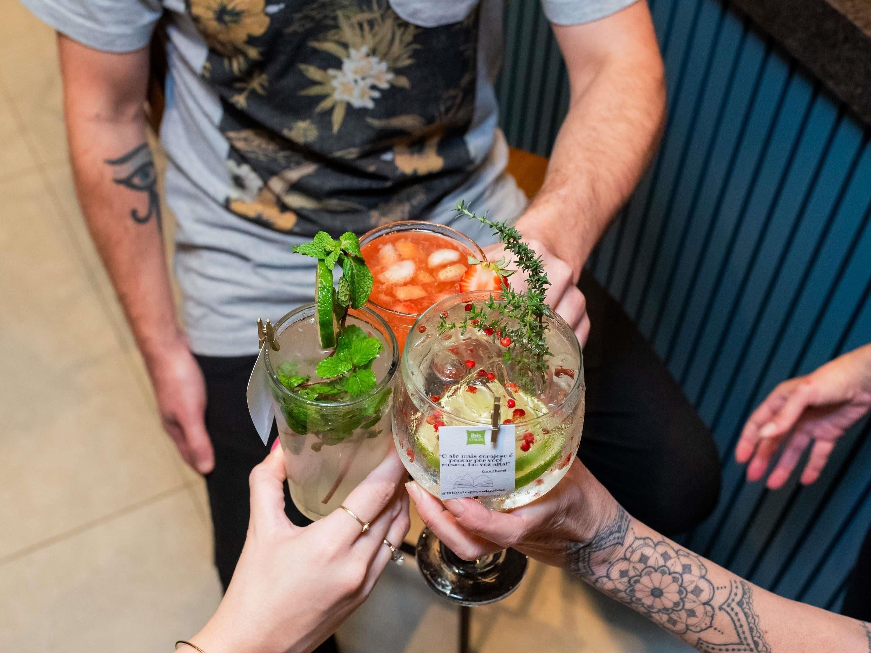 Two people holding glasses of cocktails with garnishes.