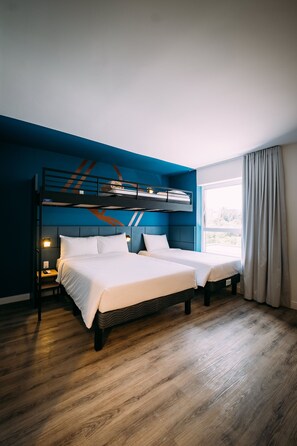 Habitación con dos camas, una litera, suelo de madera, ventana con cortinas y una mesita de noche con lámpara.