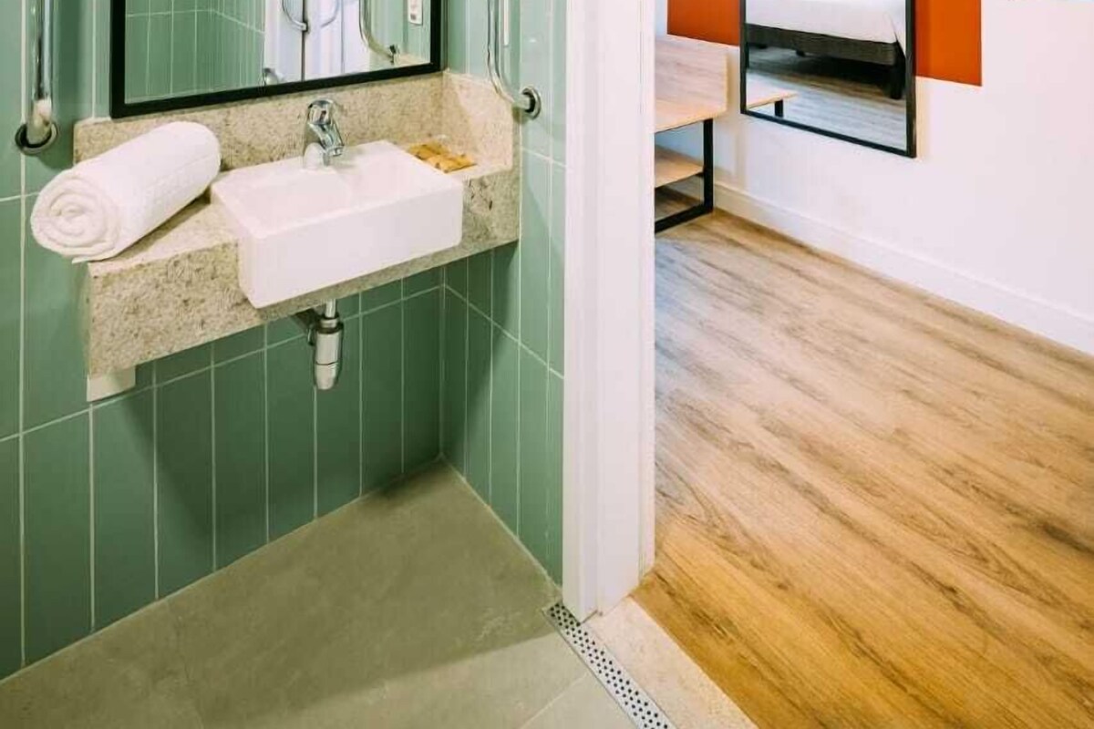 Un baño moderno con lavamanos, espejo y barras de apoyo.