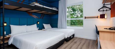 Habitación de hotel moderna con dos camas, un escritorio, una silla, un ventanal con vistas a zonas verdes y una litera encima de las camas.