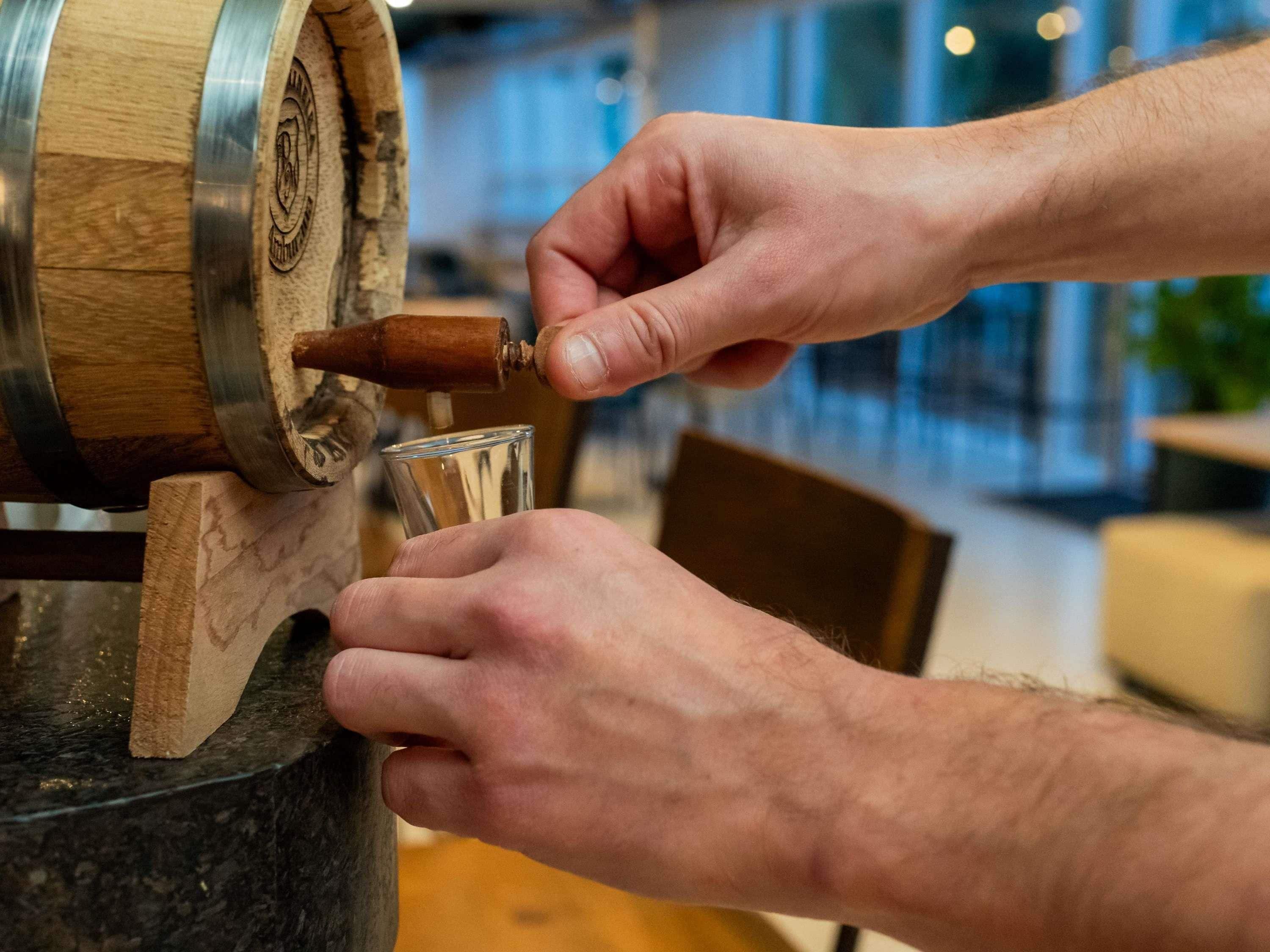 A person pouring a drink from a wooden barrel tap into a glass.