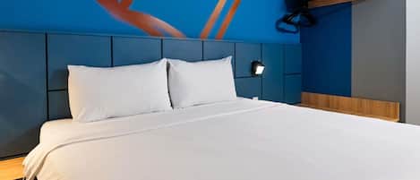 A hotel room with a large bed, a headboard with a geometric design, a wall-mounted shelf with towels, and a wall art piece.