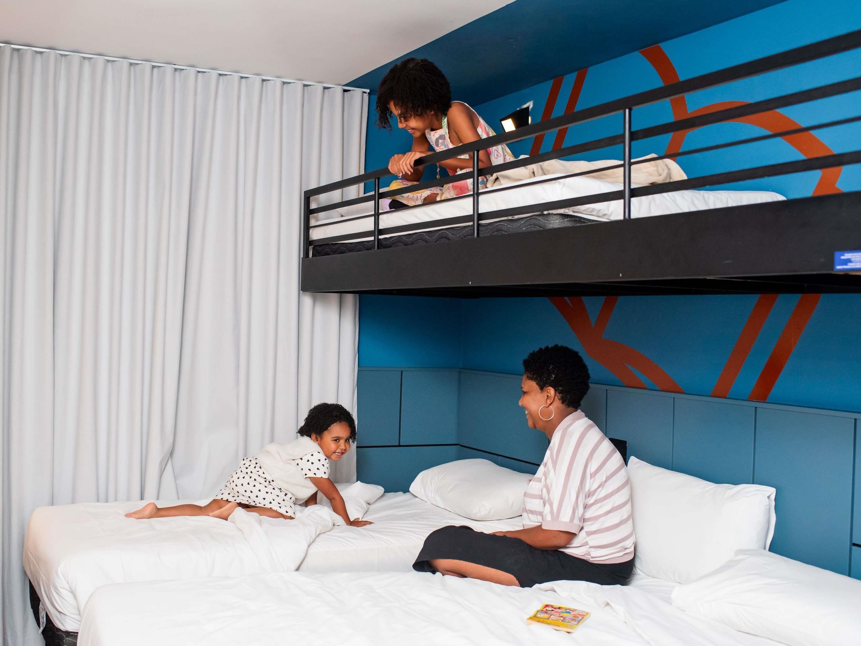 A hotel room with a bunk bed, a lower bed, and a blue accent wall.