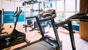 A gym with cardio equipment, weight machines, and a TV screen.