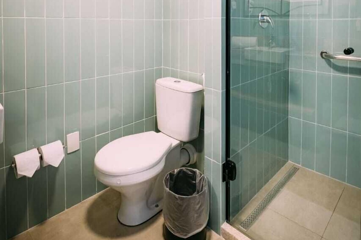 Un baño con inodoro, cubo de basura, cabina de ducha de vidrio y barra para toallas.