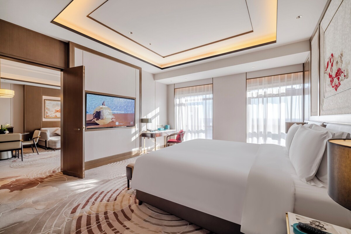 A hotel room with a large bed, a desk, a chair, and a television.