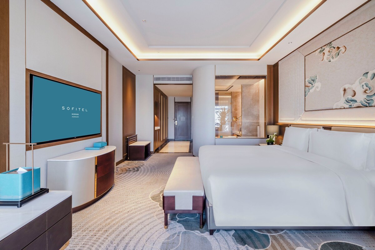 A modern hotel room with a large bed, a flat-screen TV, a bedside table, and a bench.