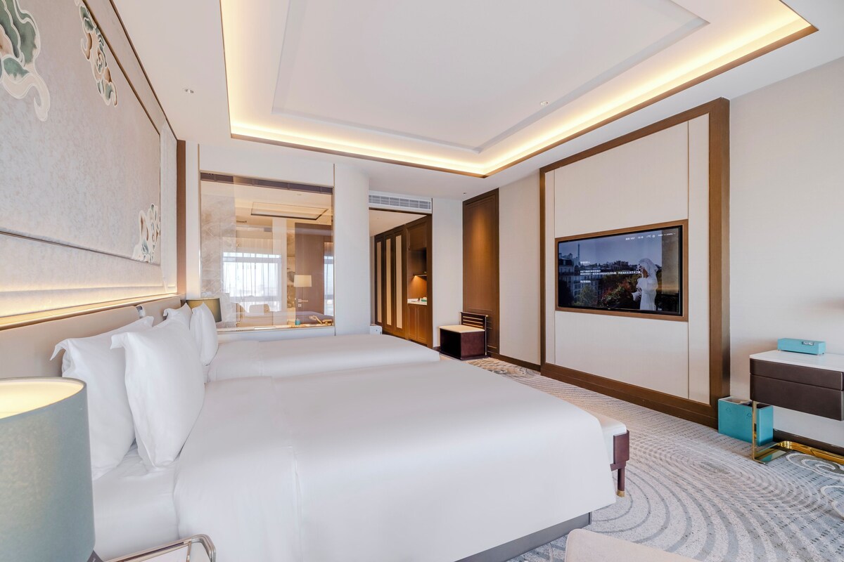 A modern hotel room with a large bed, a television, and a desk with a lamp.