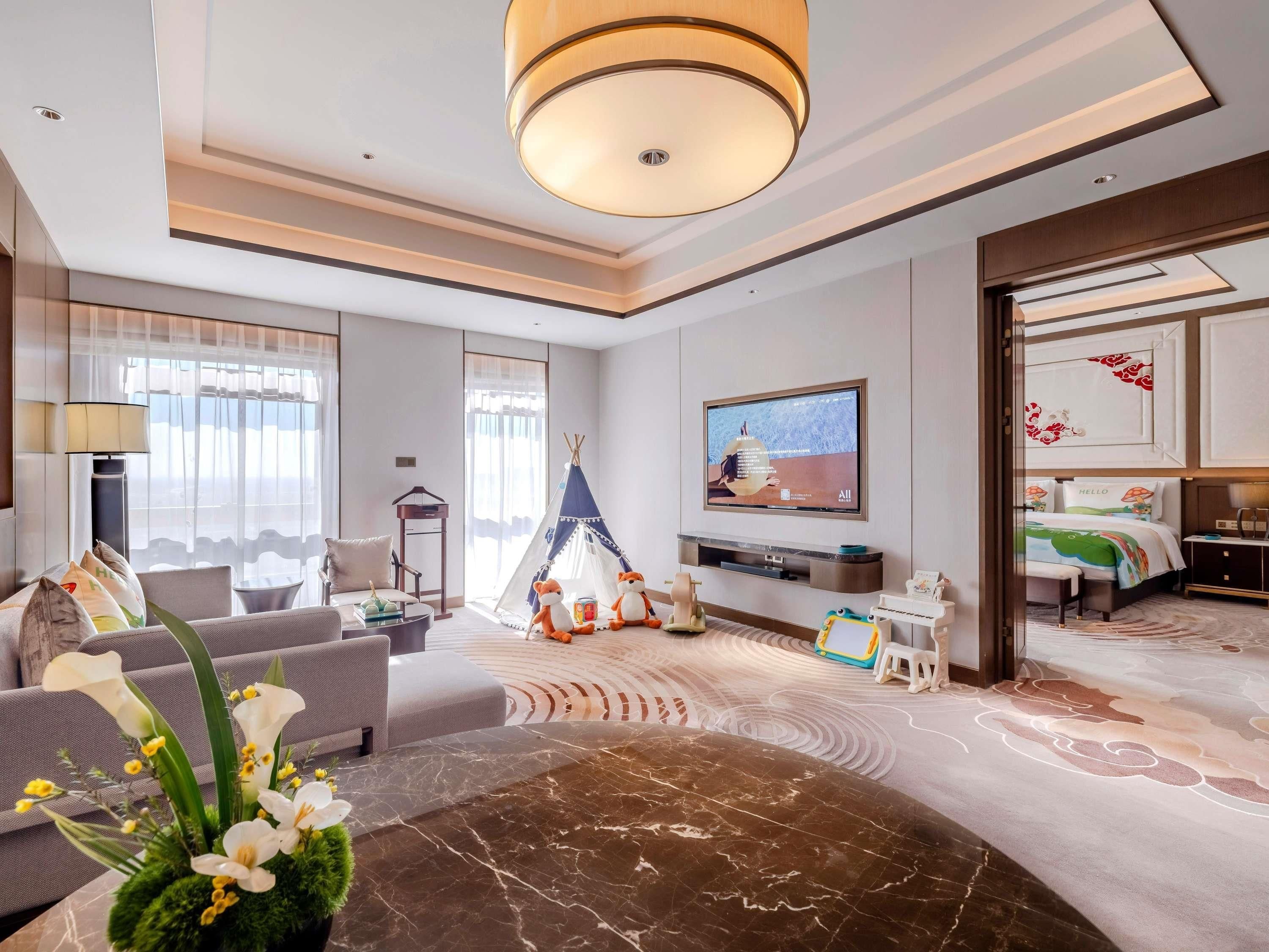 A modern hotel room with a sofa, a coffee table, a television, a bed, and a tent.