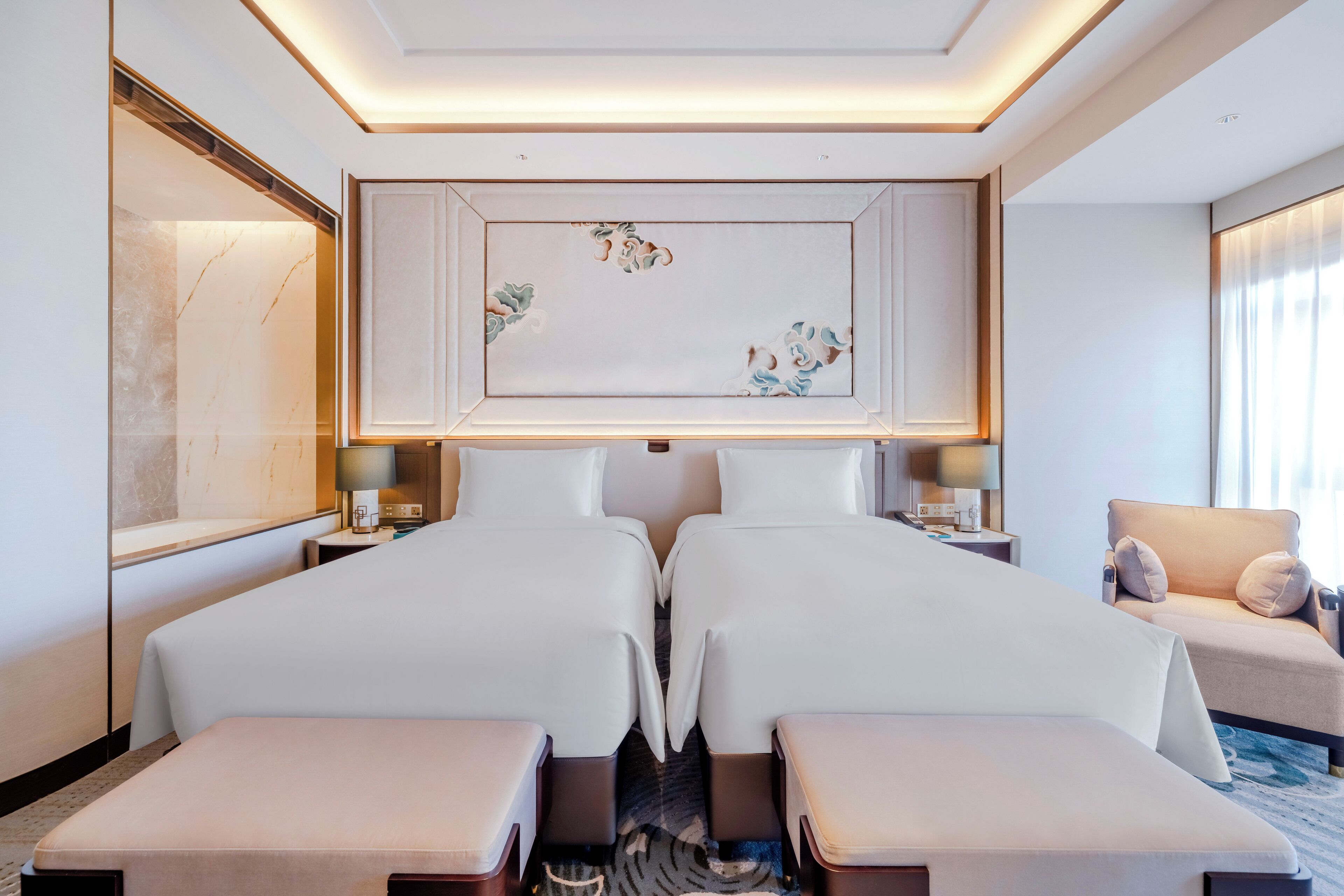 A hotel room with two beds, a sofa, a large artwork on the wall, and a view of the city.