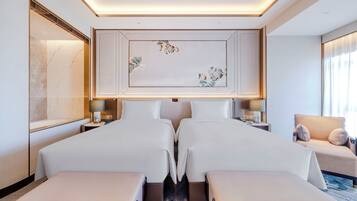 A hotel room with two beds, a sofa, a large artwork on the wall, and a view of the city.