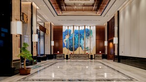 A spacious lobby with a polished marble floor, a large abstract painting on the back wall, and a reception desk with a potted plant.