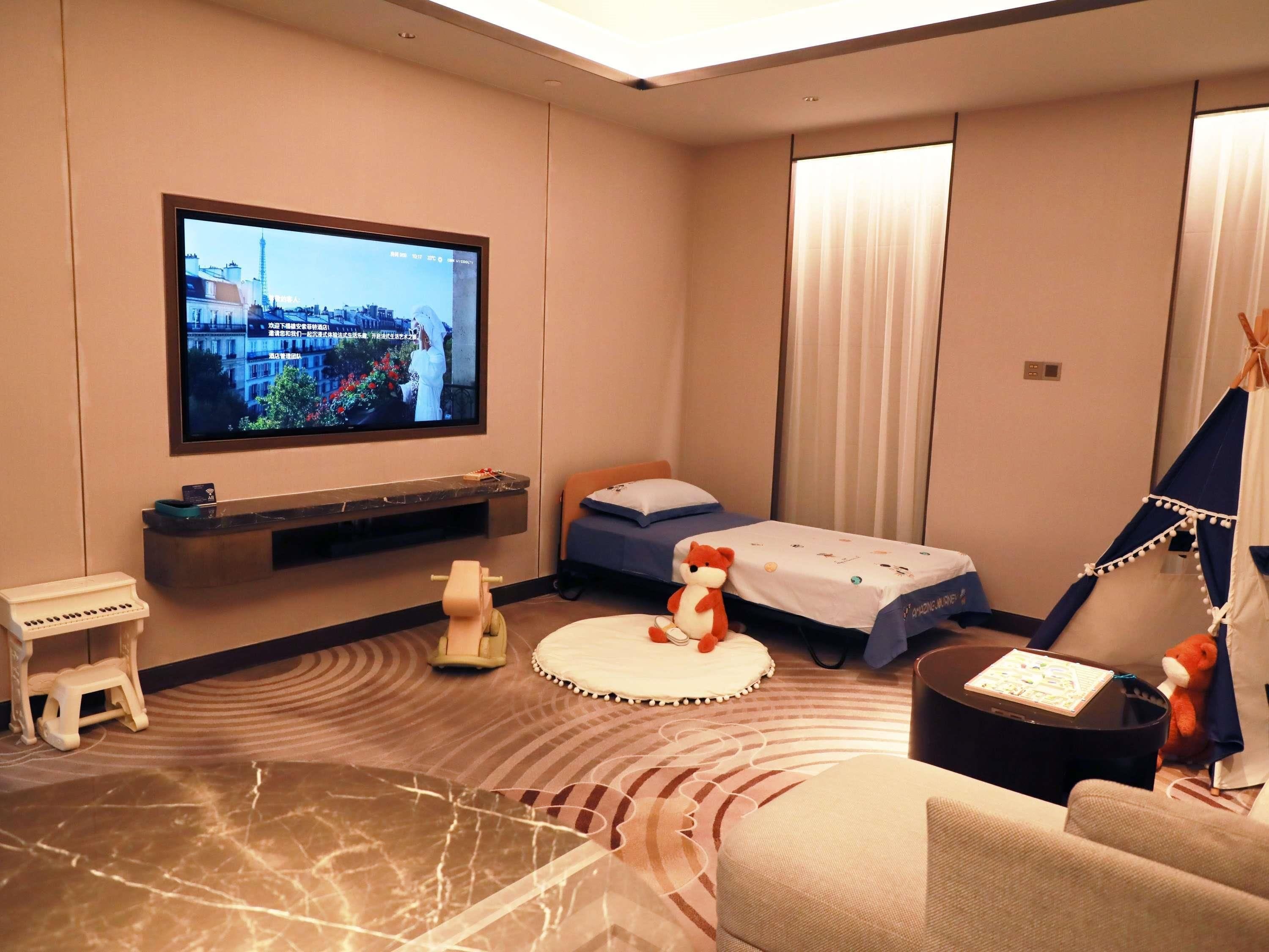 A hotel room with a bed, a TV, a small table, a chair, and a teddy bear.
