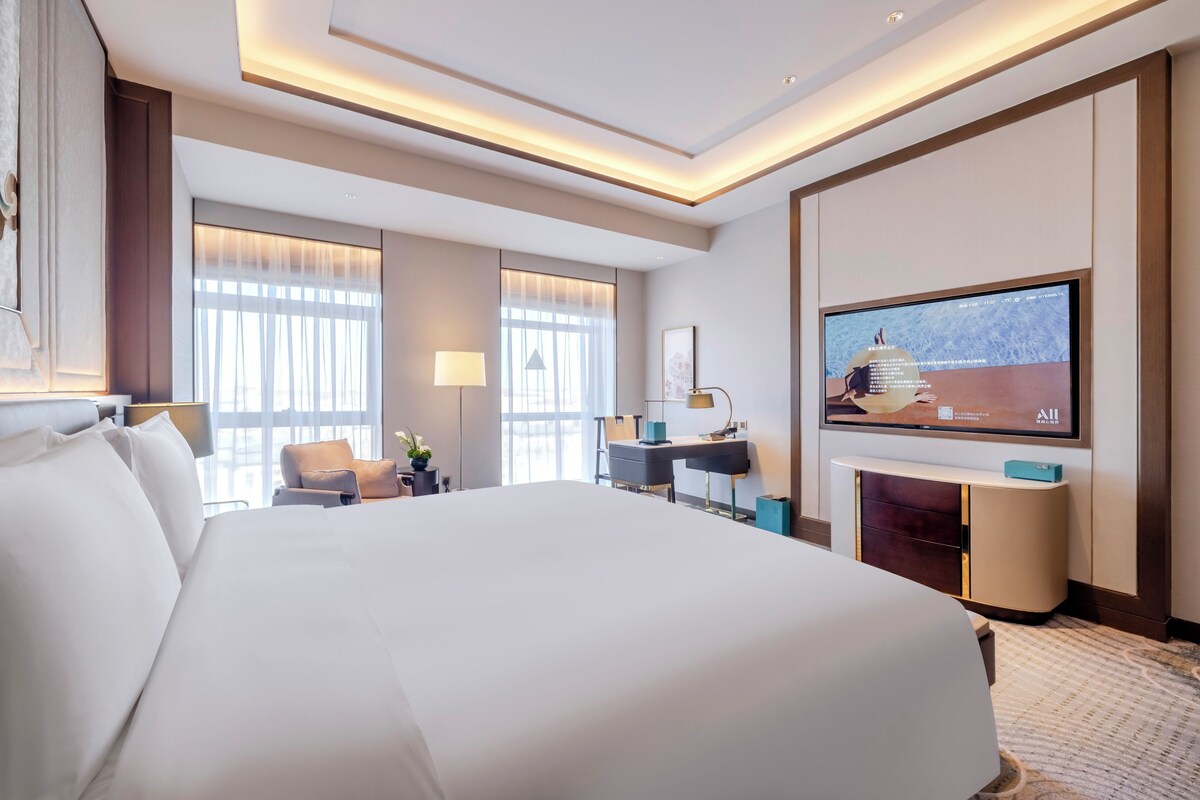 A hotel room with a large bed, a desk, a TV, and a fireplace.