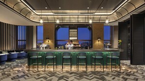 A bar area with a counter, stools, and a view of the cityscape through large windows. - Sofitel Xiong An (Baoding)