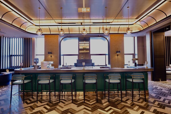 A modern bar area with a green bar counter, four bar stools, and pendant lighting.