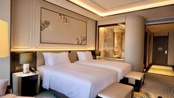 A hotel room with two beds, a nightstand with a lamp, a mirror, and a carpeted floor.