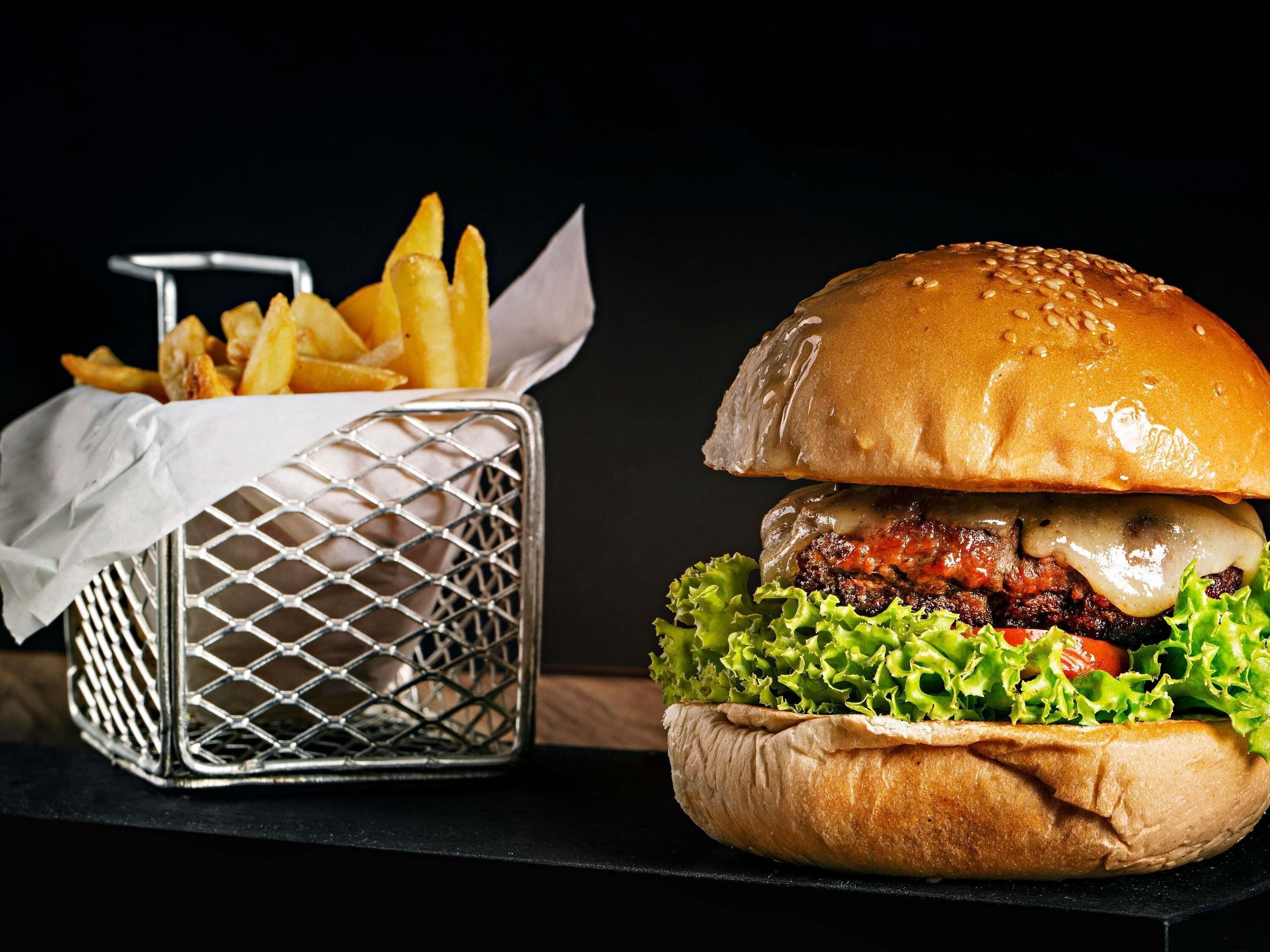 Een hamburger en een mand met frietjes op een zwarte tafel.