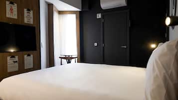 Habitación de hotel con una cama grande, una mesita pequeña y una puerta. Se observan decoraciones en la pared y un equipo de aire acondicionado.
