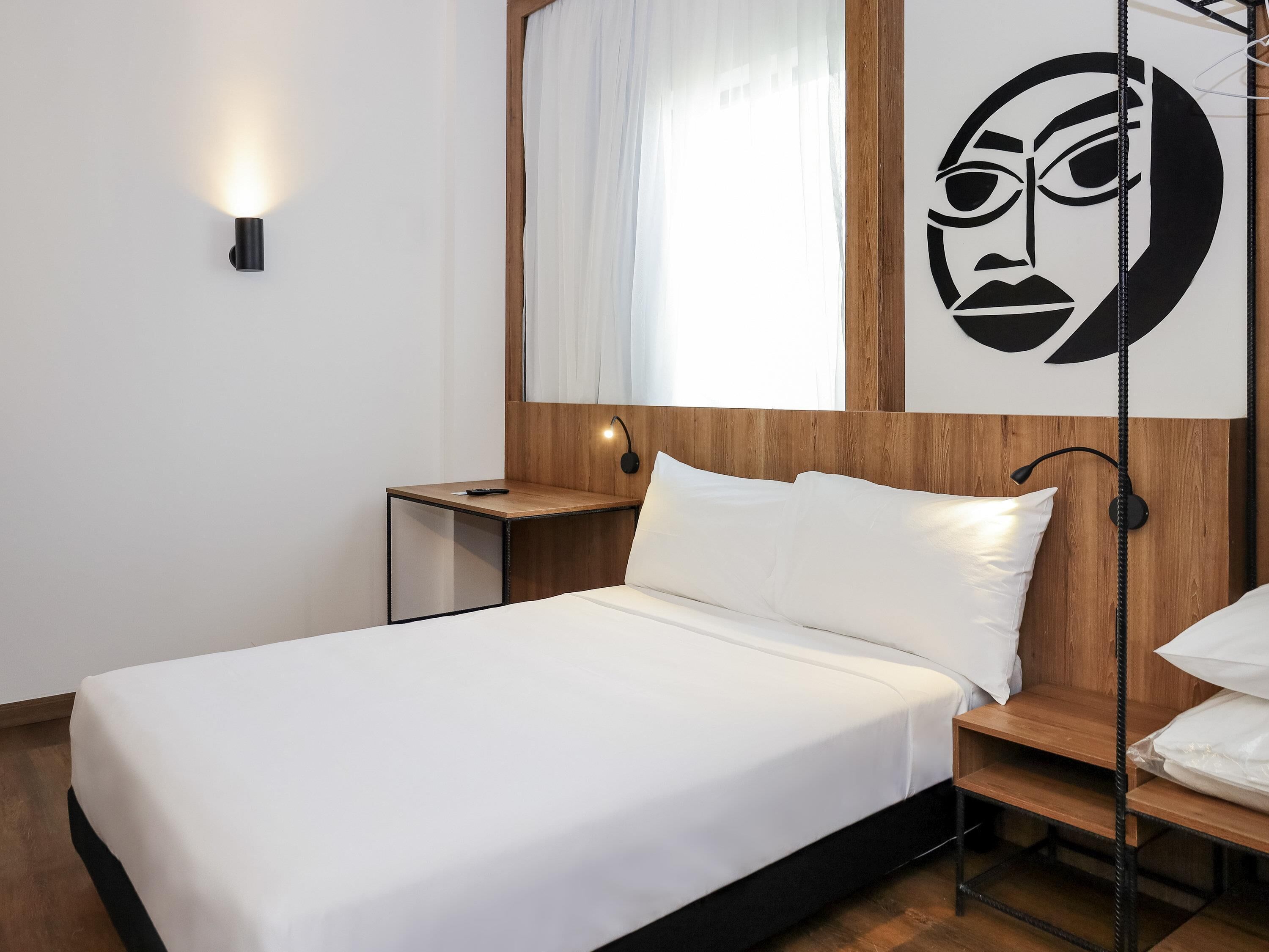 A neatly made bed with white linens, a wooden headboard, a bedside table with a lamp, and a wall-mounted artwork.