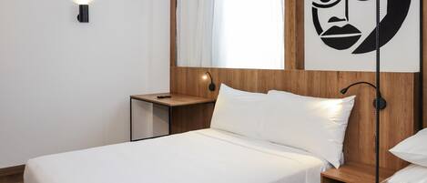 A neatly made bed with white linens, a wooden headboard, a bedside table with a lamp, and a wall-mounted artwork.