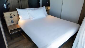 A neatly made bed with white linens, a bedside table with a lamp, and a wooden nightstand.