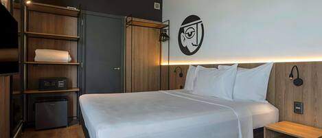 Una habitación de hotel moderna con una cama grande, un armario de madera, estanterías empotradas y una lámpara fijada a la pared.