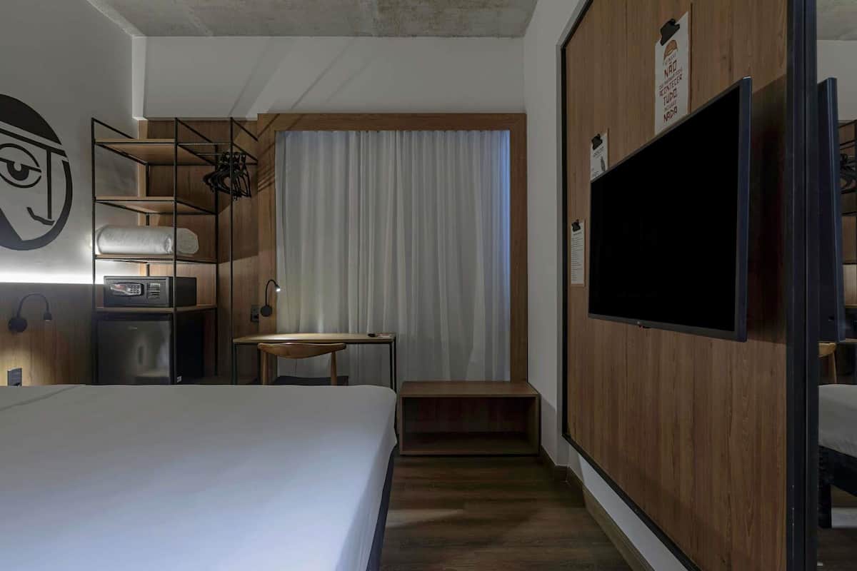 Una habitación de hotel con cama, escritorio, silla, televisión y armario.