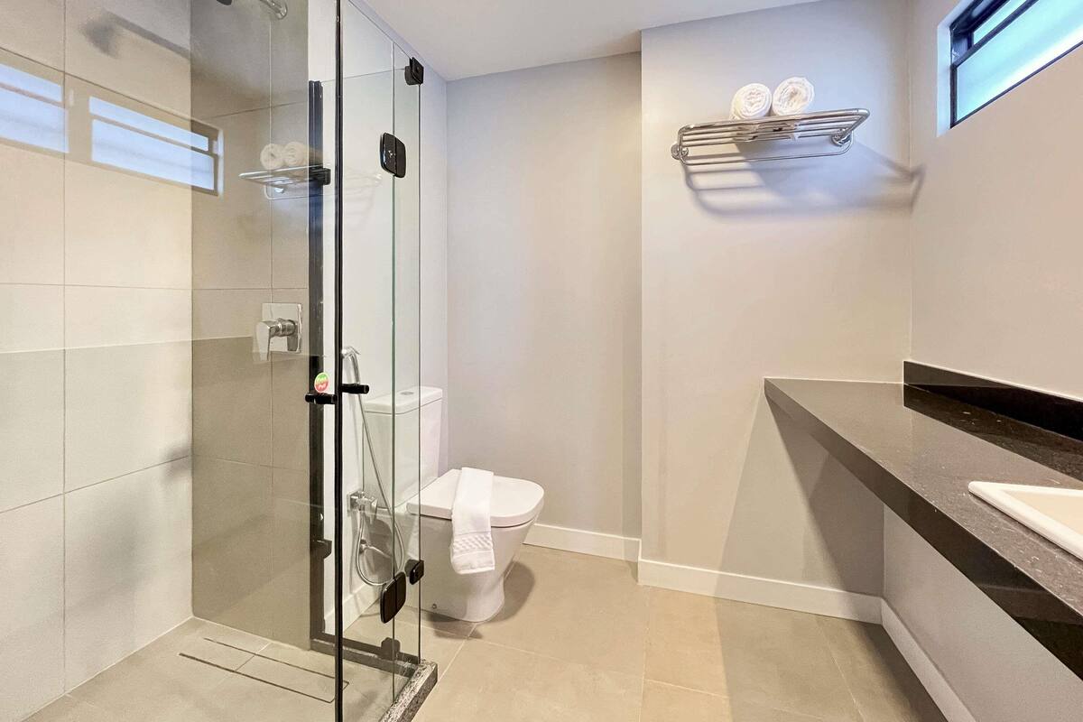 Un baño moderno con ducha envuelta en vidrio, inodoro blanco y tocador con lavabo.