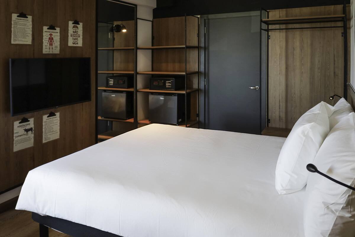 A neatly made bed with white linens, a wooden floor, and a wardrobe with a mirror and shelves.