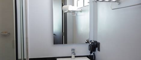 A modern bathroom with a glass shower enclosure, a white sink, a mirror, and a towel rack with towels.