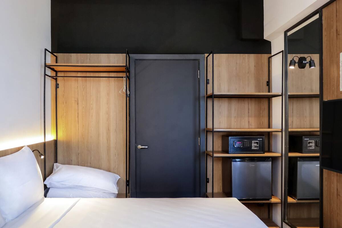 A compact hotel room with a bed, a wardrobe, a desk with a computer, and a small kitchenette.