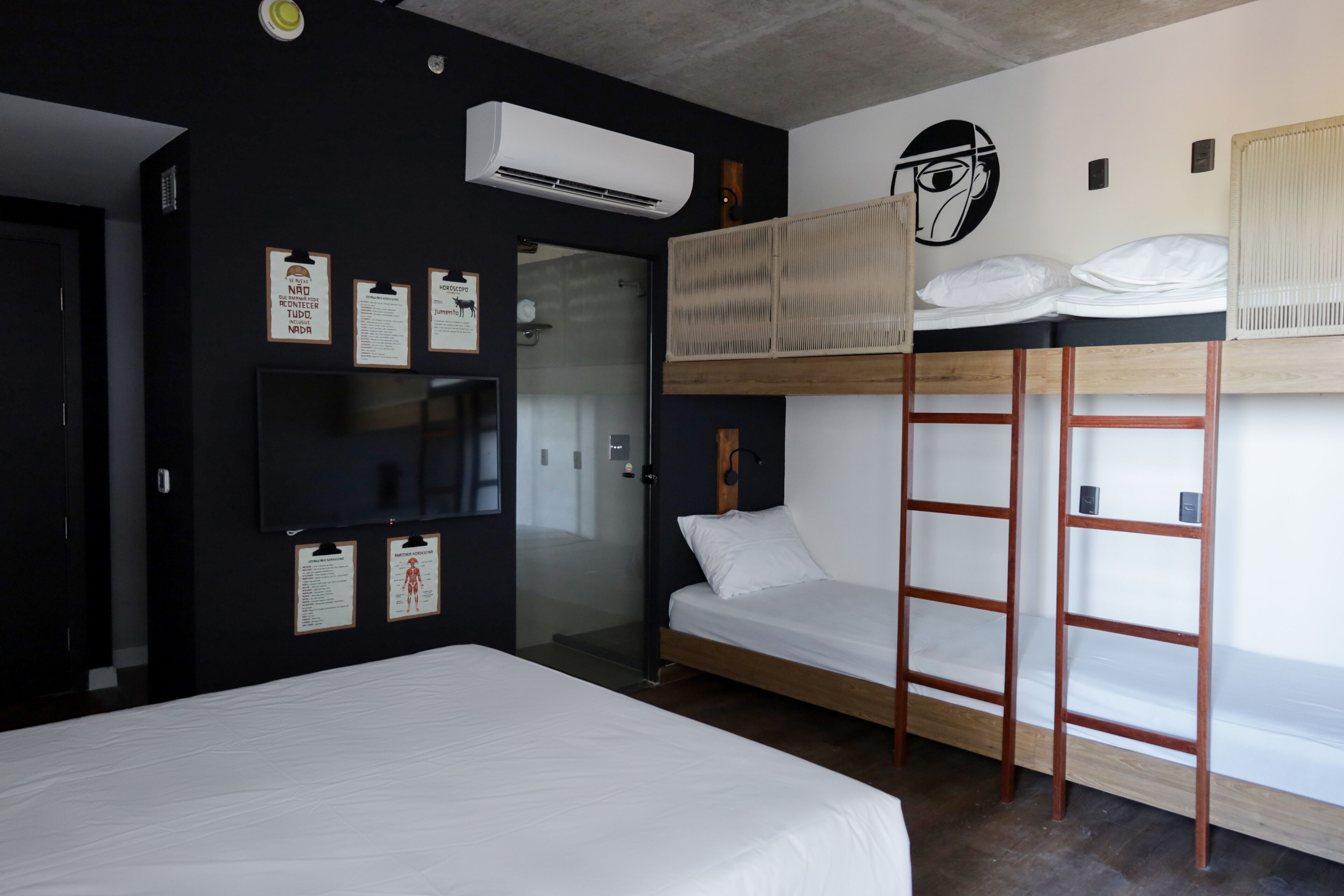 Habitación de hotel con literas, cama plana, televisor y aire acondicionado instalado en la pared.