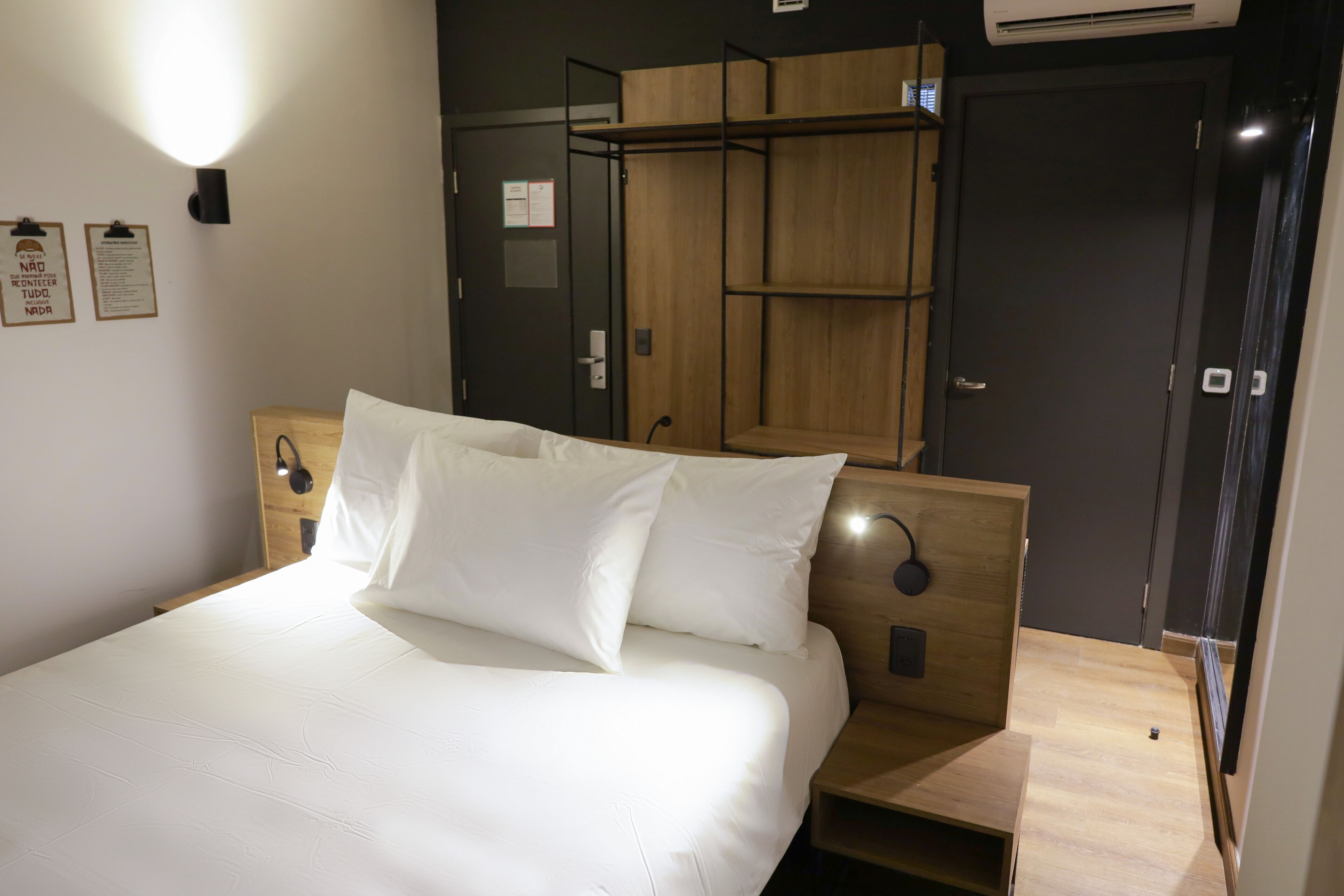 A neatly made bed with white linens in a modern room with wooden furniture and a built-in wardrobe.