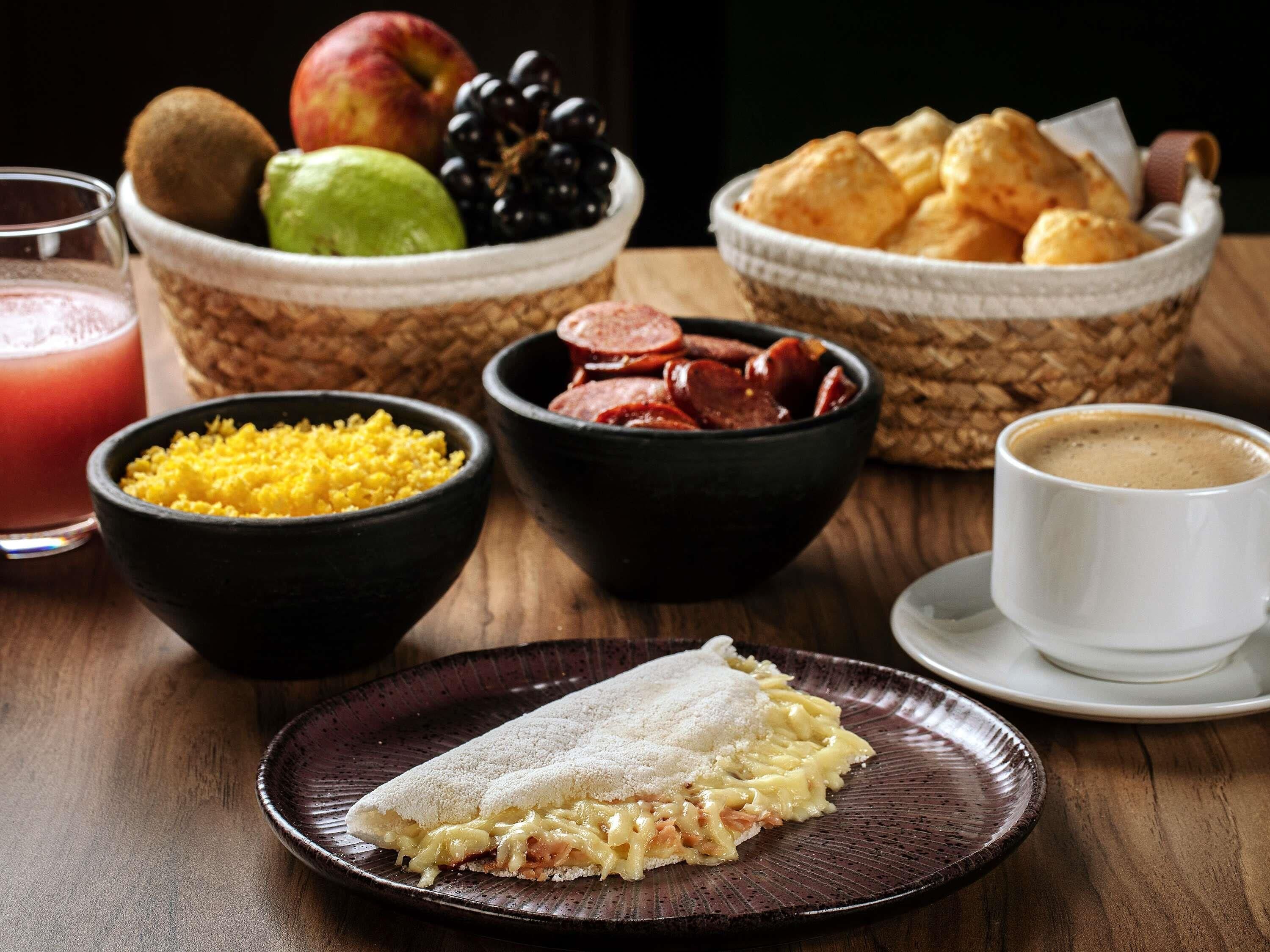 A breakfast setting with a plate of food, bowls of fruits and condiments, and a cup of coffee.