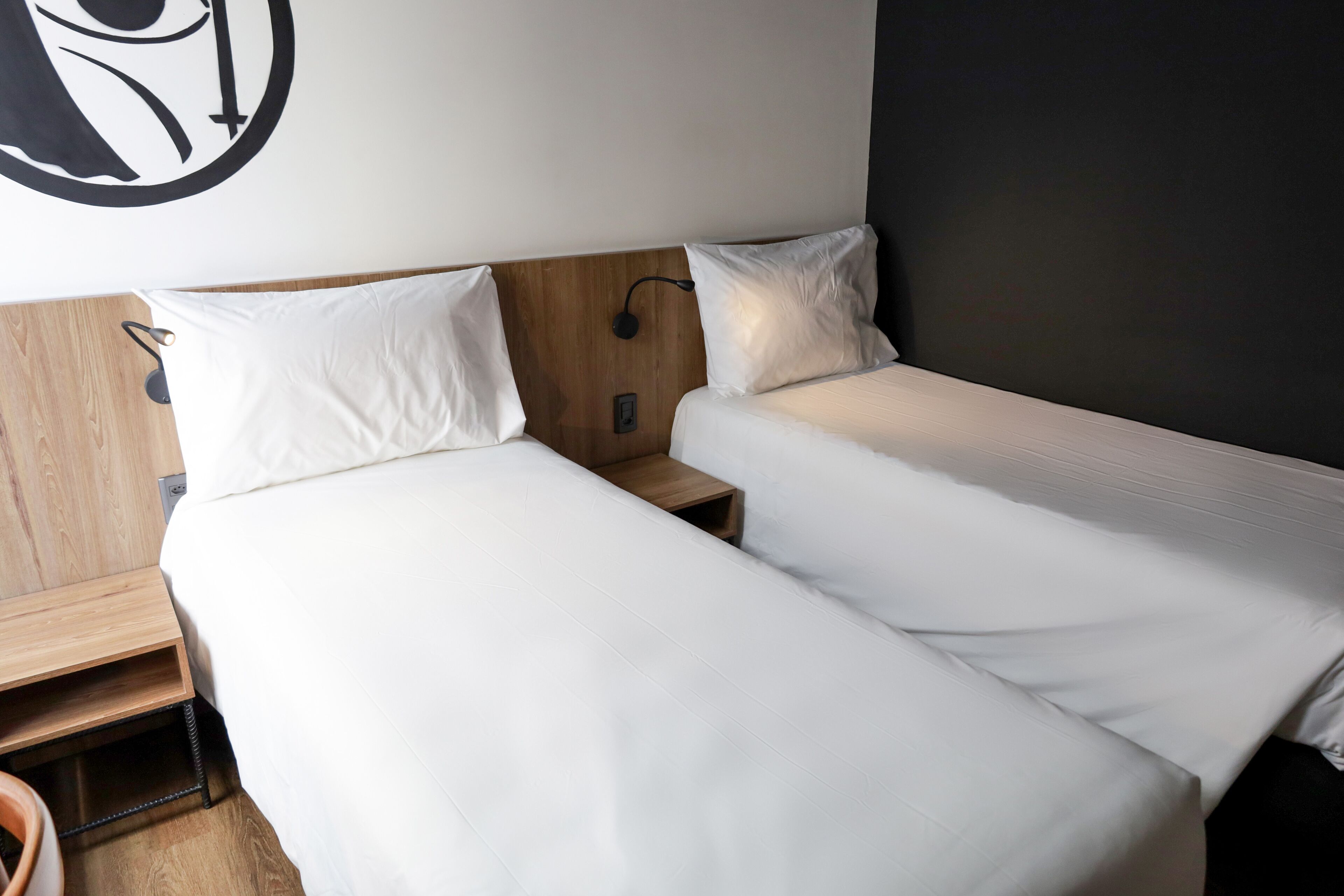 Une chambre d’hôtel avec deux lits simples, des têtes de lit en bois et un luminaire fixé au mur.