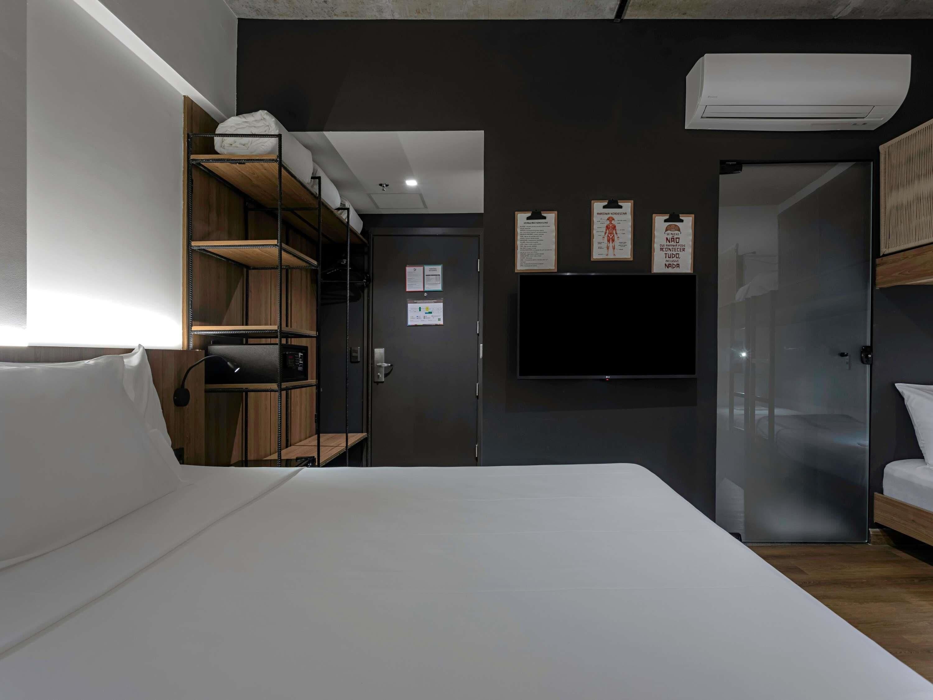 A modern hotel room with a bed, a TV, a wardrobe, and a door leading to another room.