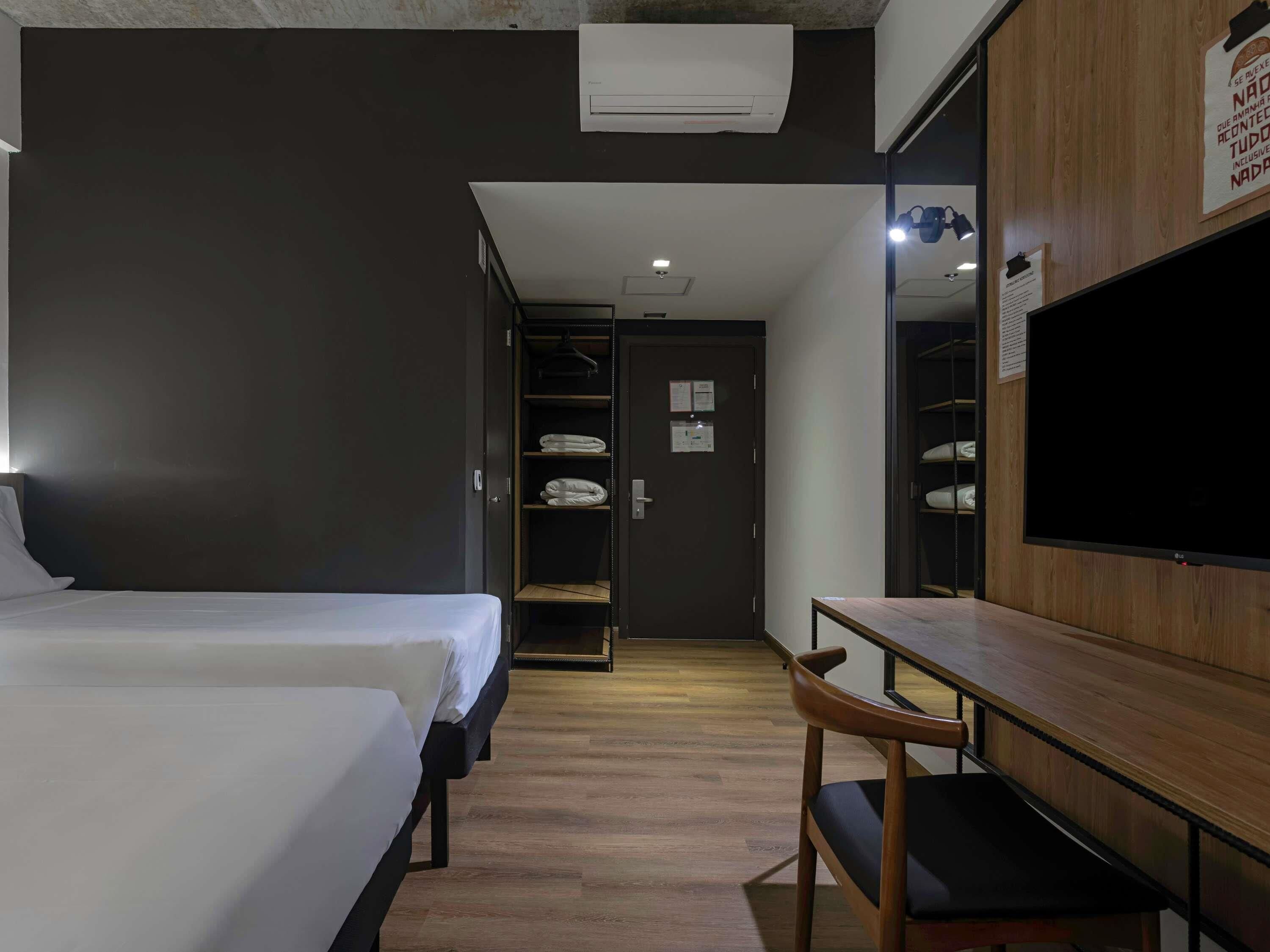 A hotel room with a bed, a desk, a chair, a wardrobe, and a television.