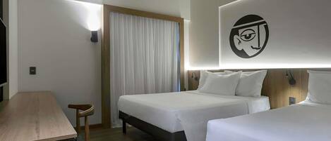 Habitación de hotel con dos camas, un escritorio, una silla, una cortina y una lámpara fijada a la pared.