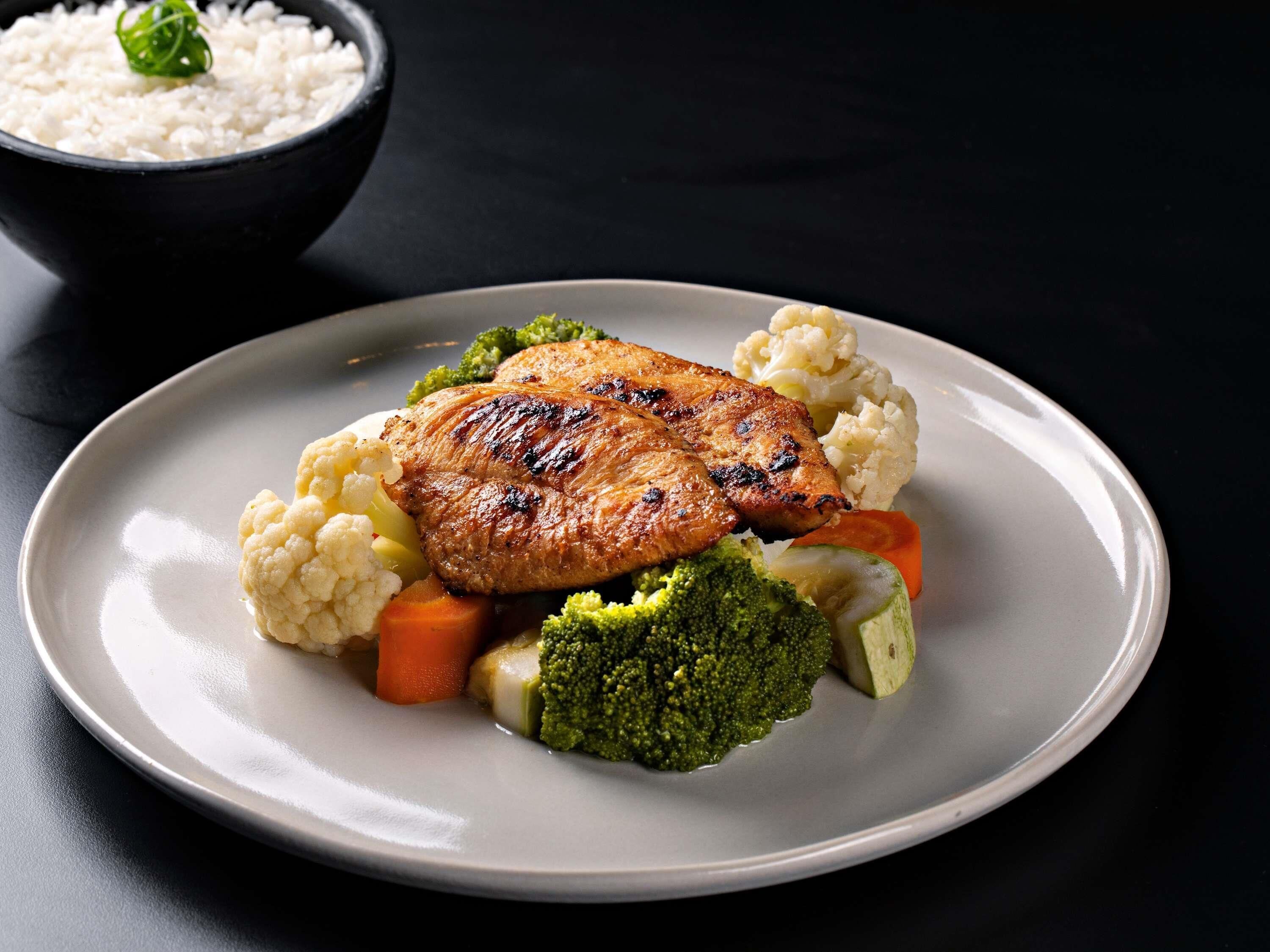 Een bord met gegrild vlees, bloemkool, wortels en broccoli.