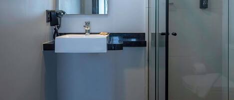 Un baño moderno con un lavamanos blanco, una cabina de ducha con mampara de vidrio y un toallero negro.