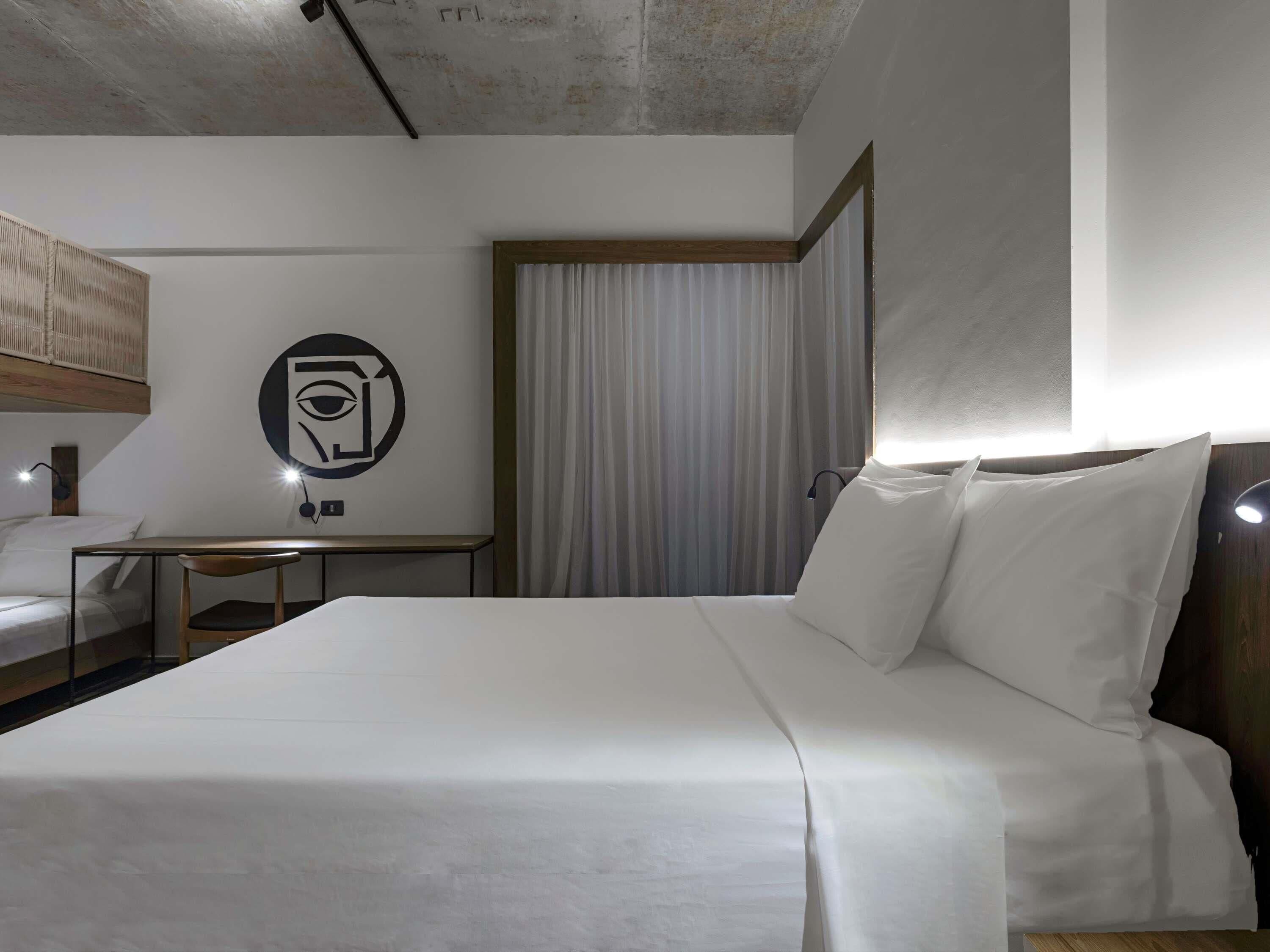 Een hotelkamer met een groot bed, een bureau, een stoel, een kunstwerk aan de muur en een raam met gordijnen.