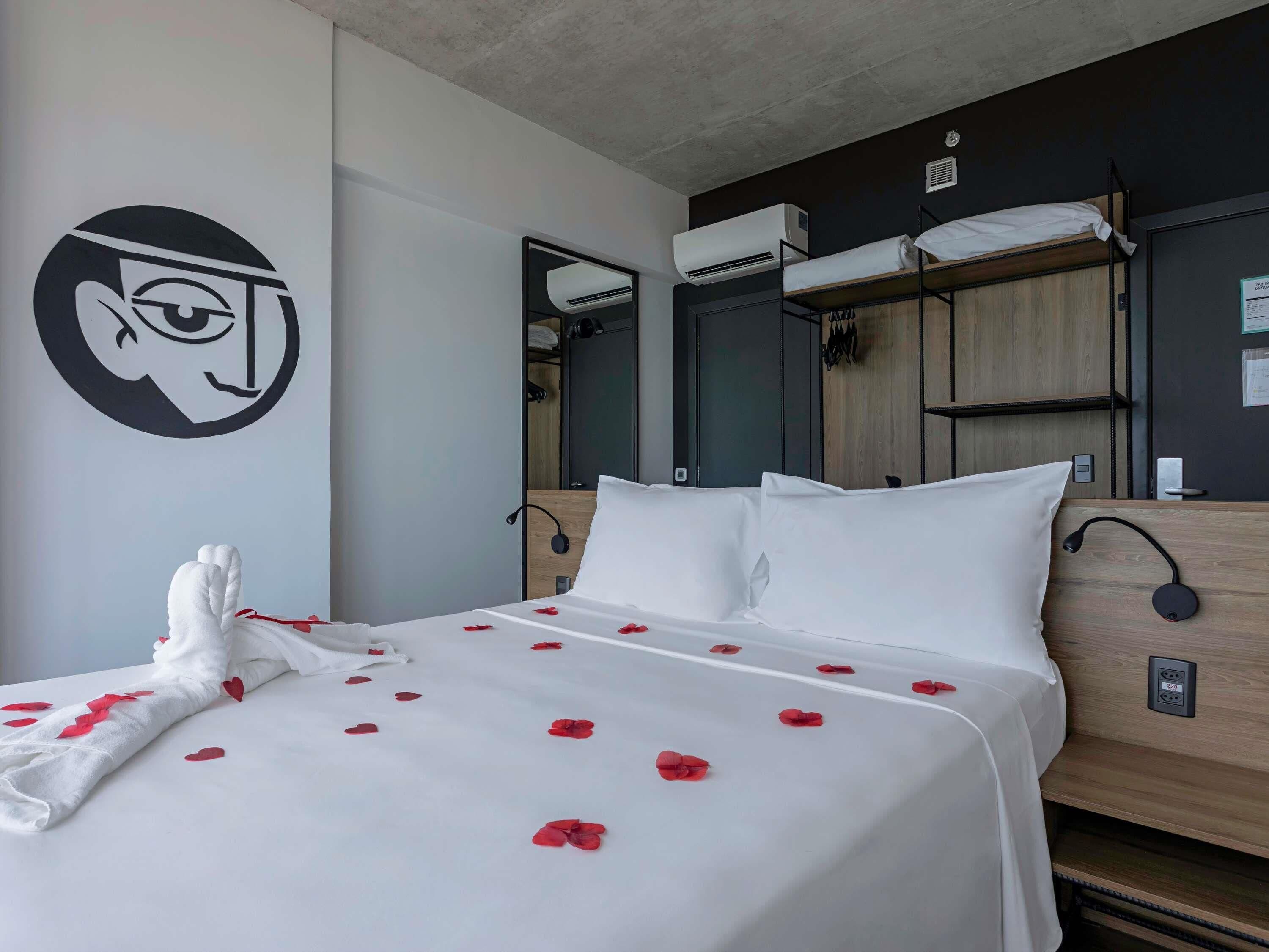 A hotel room with a bed, a wall-mounted air conditioner, a wooden wardrobe, and a mirror.
